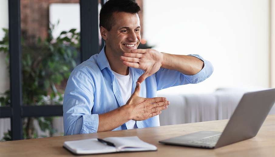 Happy smiling deaf young caucasian man uses sign language while video call using laptop while sitting at home, virtual communication concept Happy smiling deaf young caucasian man uses sign language while video call using laptop while sitting at home, virtual communication concept